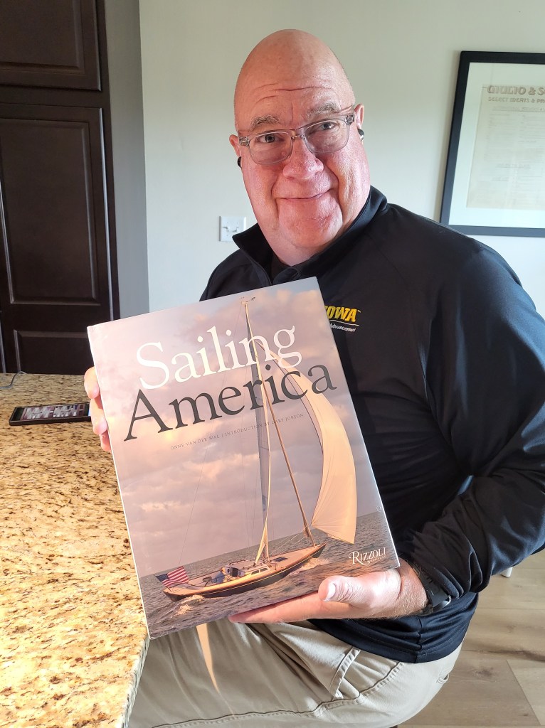 Kent holding the beautiful coffee table book, Sailing America by Onne van der Wal, awarded to him by Offshore Sailing School.