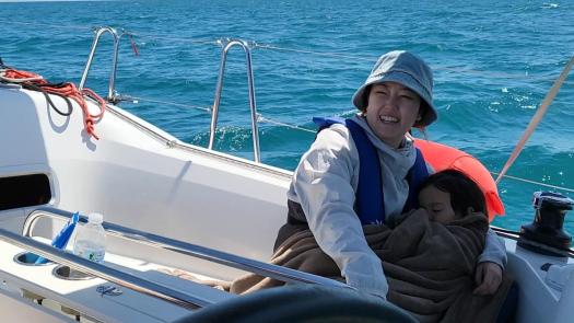 in the cockpit of sailboat, a woman holds child in her arms as he sleeps 