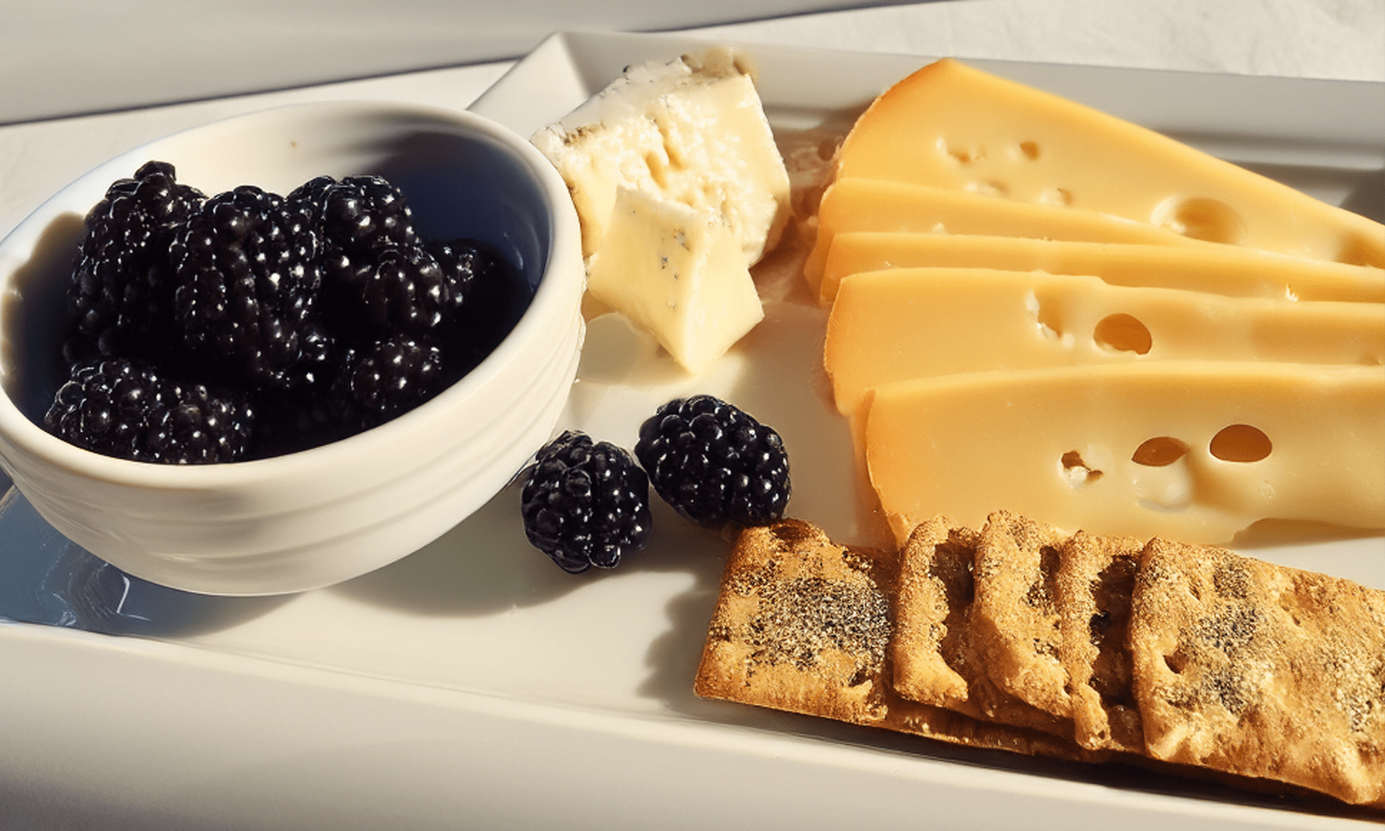 Cheese, blackberries, and crackers on a plate