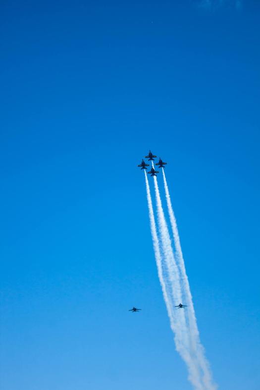 four Blue Angels jets flying upward in formation with trails of smoke behind them