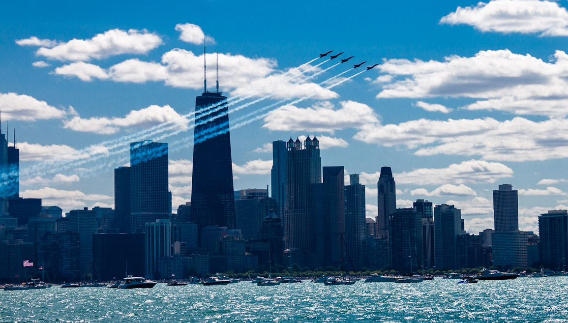 five Blue Angel jets climbing high into the sky above the Chicago skyline, smoke trailing behind them