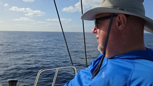 a man wearing a hat and sunglasses, looking out to the ocean horizon