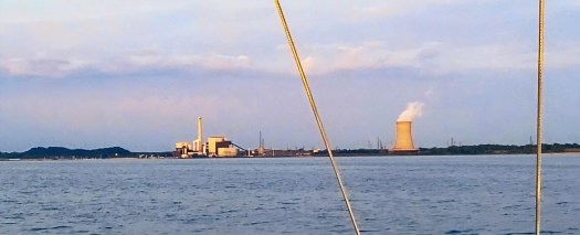 a large cooling tower on the shore with steam rolling out into the sky