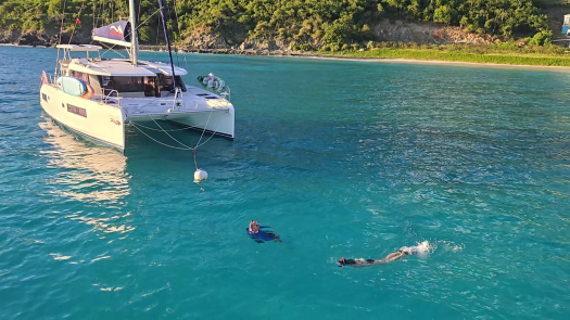 A catamaran and two snorkelers in aqua-blue waters