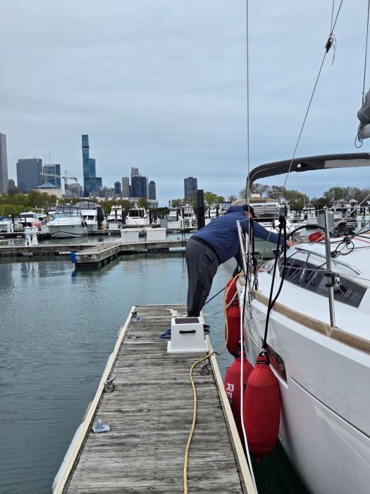 Kent standing on the dock, reaching into the cockpit of the sailboat, Chicago skyline in the background.