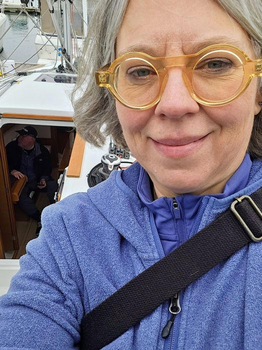 Selfie of Becca on the deck of the sailboat, showing kent through the open companionway sitting inside.