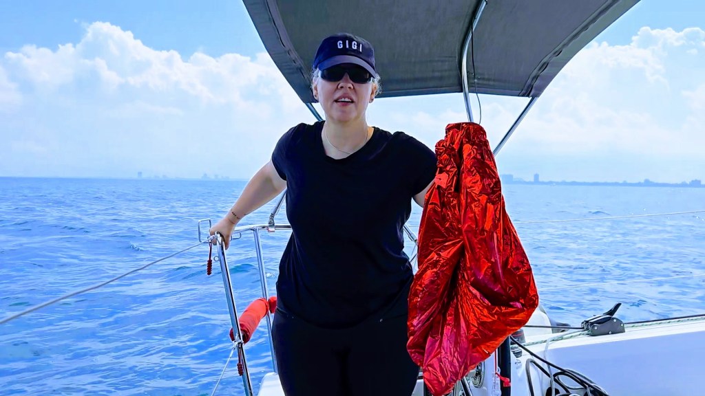 Becca holding up the large red deflated mylar balloon in the cockpit of the sailboat out on Lake Michigan.
