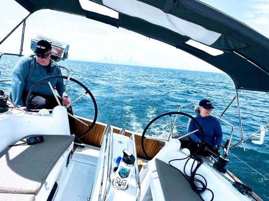 kent and becca at the helm, the boat is heeling, the skyline in the background.