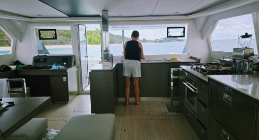 Interior of a modern sailboat galley with a person standing near the kitchen area, washing dishes.