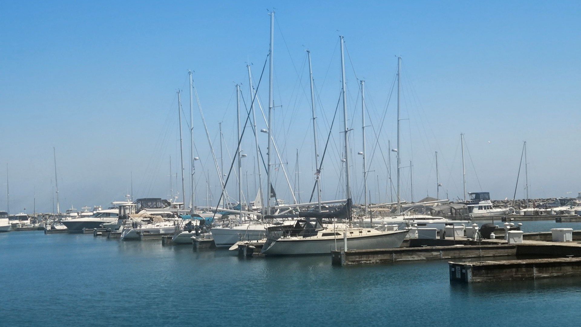 A calm, quiet Waukegan Harbor filled with docked sailboats under a clear blue sky.
