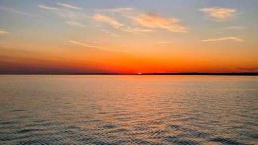 A wide, scenic shot of a sunrise over a calm body of water.