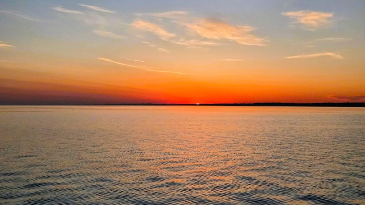 A wide, scenic shot of a sunrise over a calm body of water.